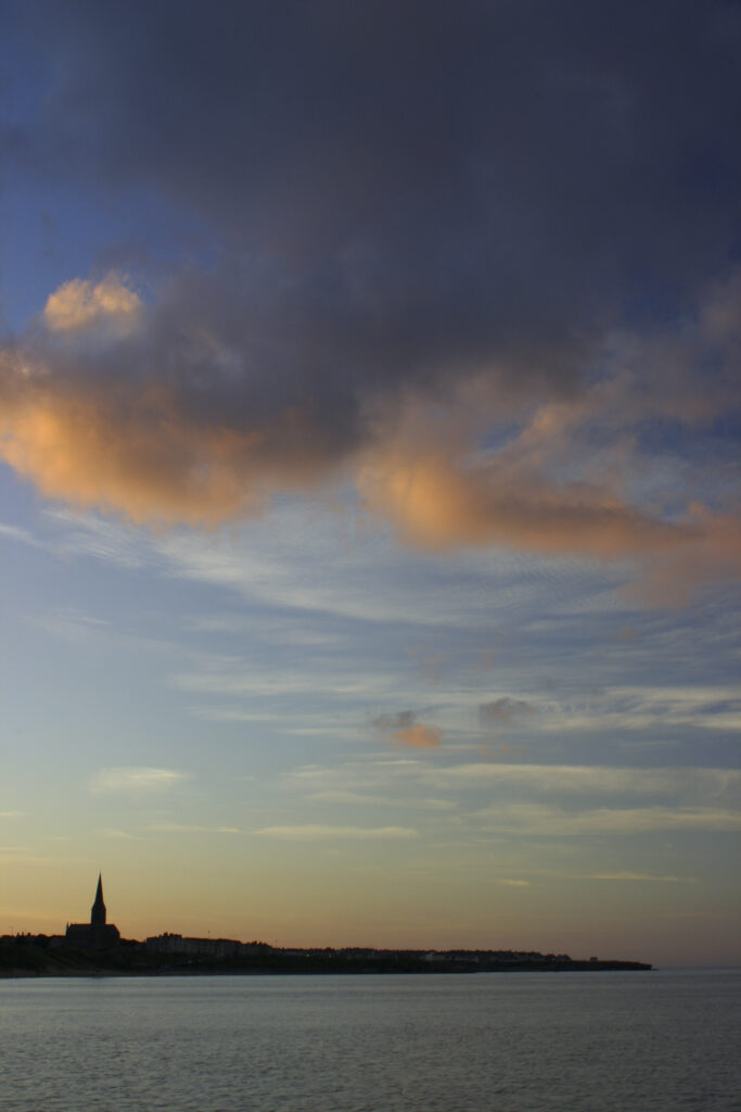 ENGLAND, Tyne & Wear, Tynemouth. The setting sun illuminates the clouds high above the long sands bay - looking towards Cullercoats