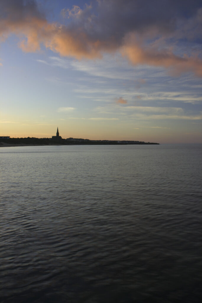 ENGLAND, Tyne & Wear, Tynemouth. The setting sun illuminates the clouds high above the long sands bay - looking towards Cullercoats