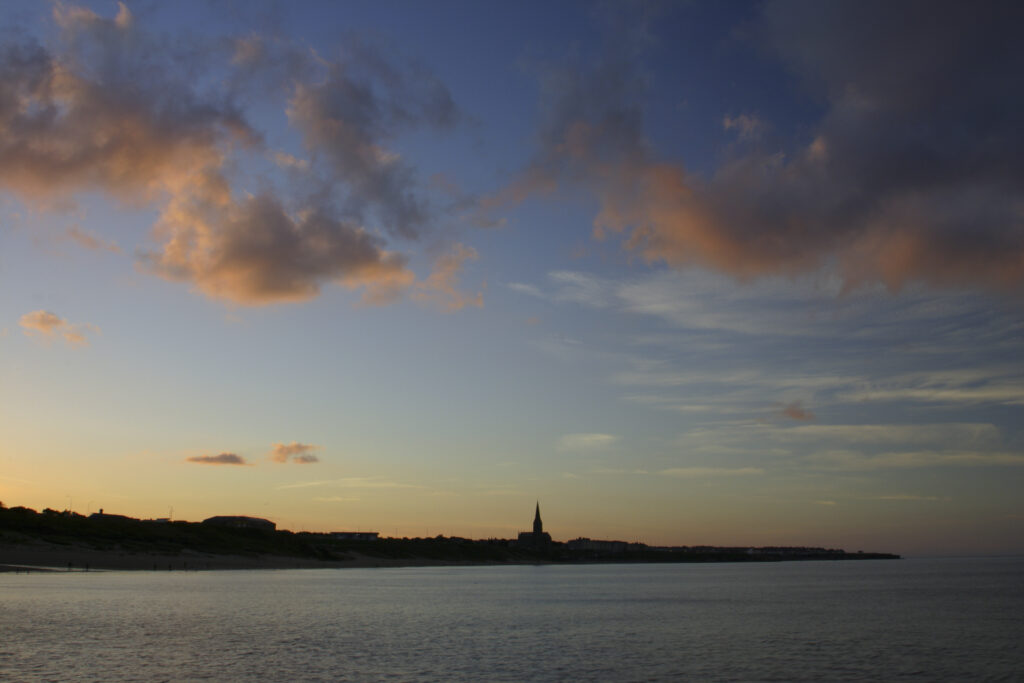 ENGLAND, Tyne & Wear, Tynemouth. The setting sun illuminates the clouds high above the long sands bay - looking towards Cullercoats