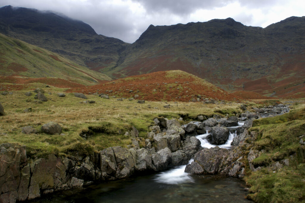 ENGLAND Cumbria Lake District National Park A small beck and red hues of the wild landscape on the Cumbria Way to Stake Pass