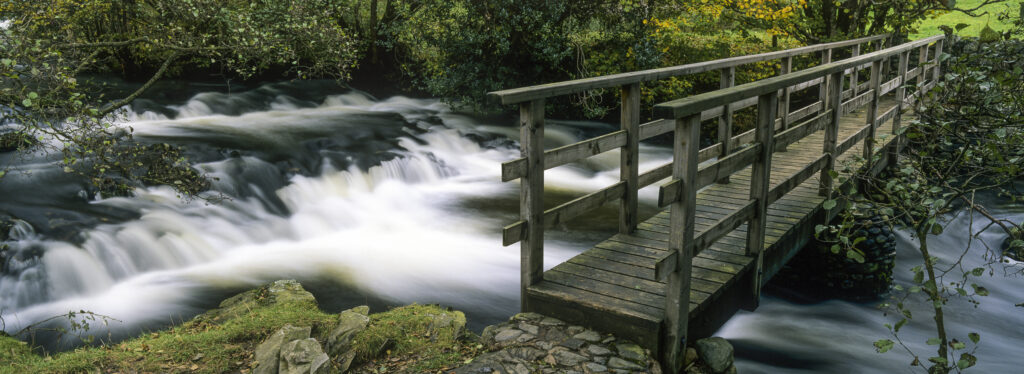 ENGLAND, Cumbria, Lake District National Park. A wooden bridge crossing across the fast waters of Torver Beck, on the 'Cumbria Way'.