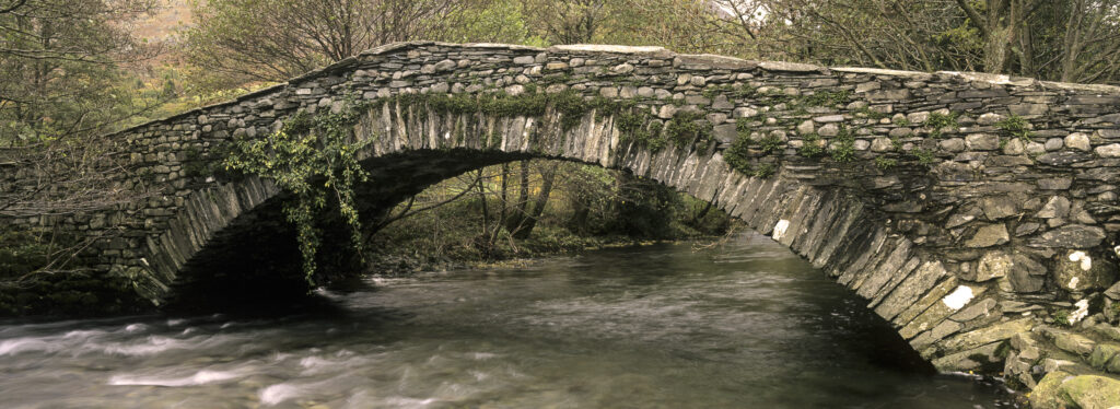 ENGLAND, Cumbria, Lake District National Park. The Cumbria Way rote passes over 'New Bridge' crossing the river Derwent in Borrowdale.