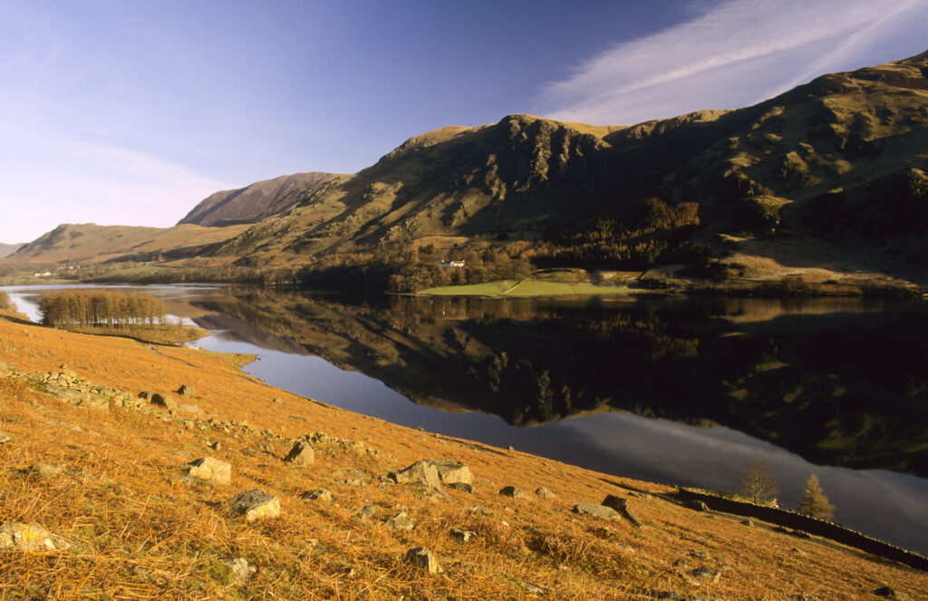 ENGLAND, Cumbria, Lake District National Park. The contrasting colours of bracken covered hills and still waters and mountains of Buttermere.