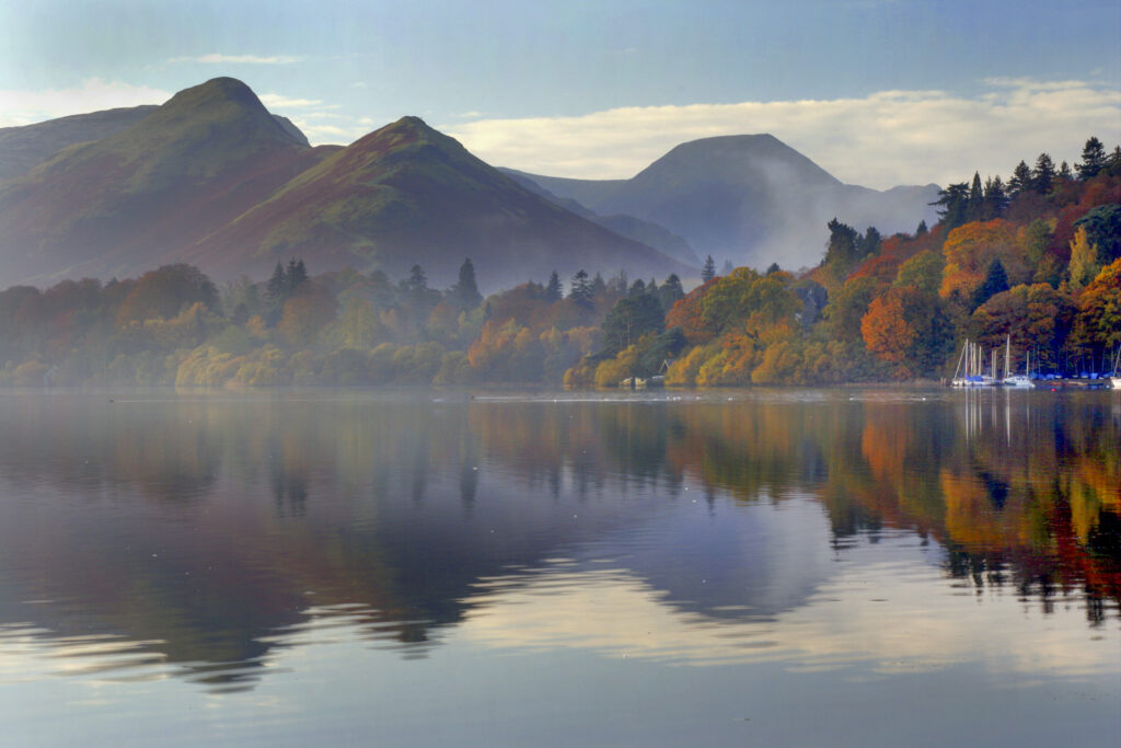 ENGLAND Cumbria Lake District National Park The surrounding autumn colours of woodland and mountain reflected in Derwentwater