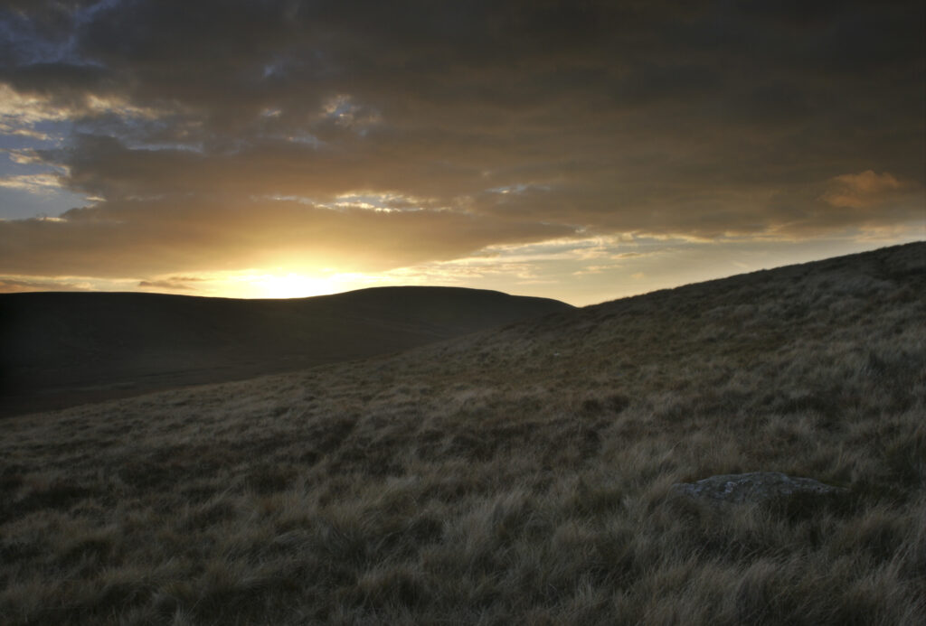 ENGLAND, Cumbria, Lake District National Park. The soft hues of a sunset behind the hills of Caldbeck common