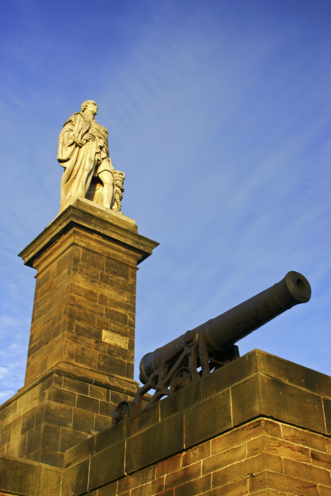 ENGLAND, Tyne and wear, Tynemouth. The setting sun iluminates the Collingwood monument and cannons