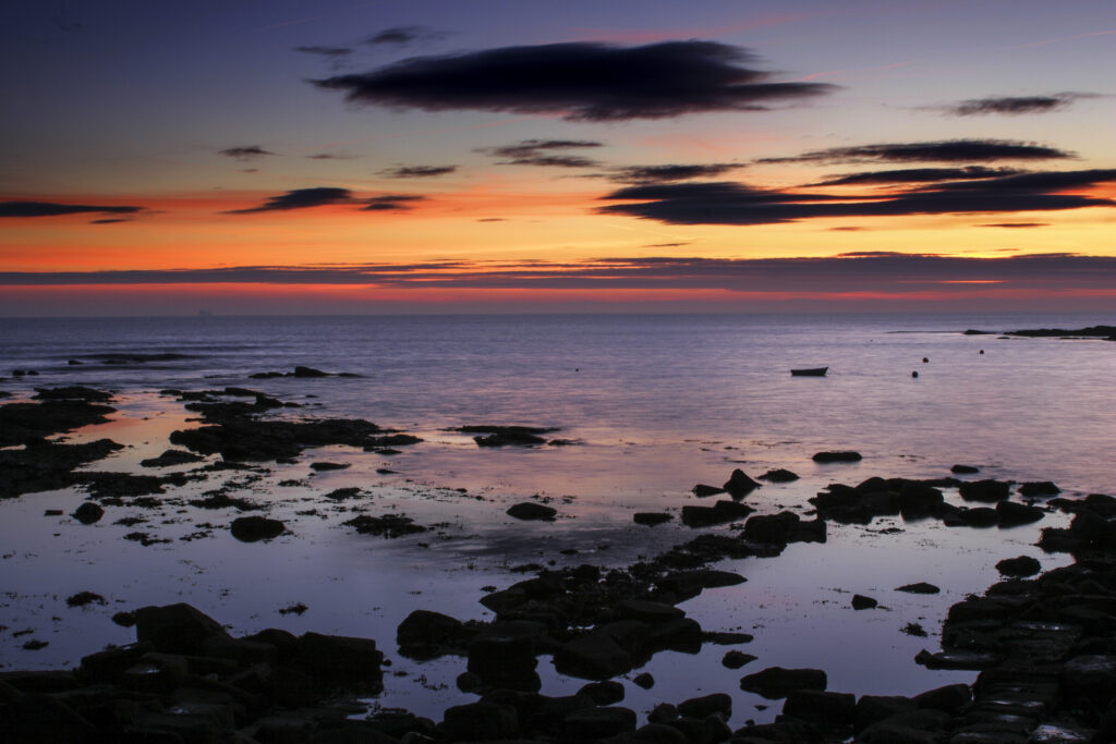 England, Tyne and Wear, Cullercoats. A colourful sunrise reflects in the still waters of the North Sea
