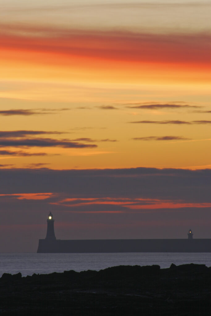 England, Tyne and Wear, Cullercoats. Sunrise looking towards the North Tyne Pier and lighthouse in Tynemouth