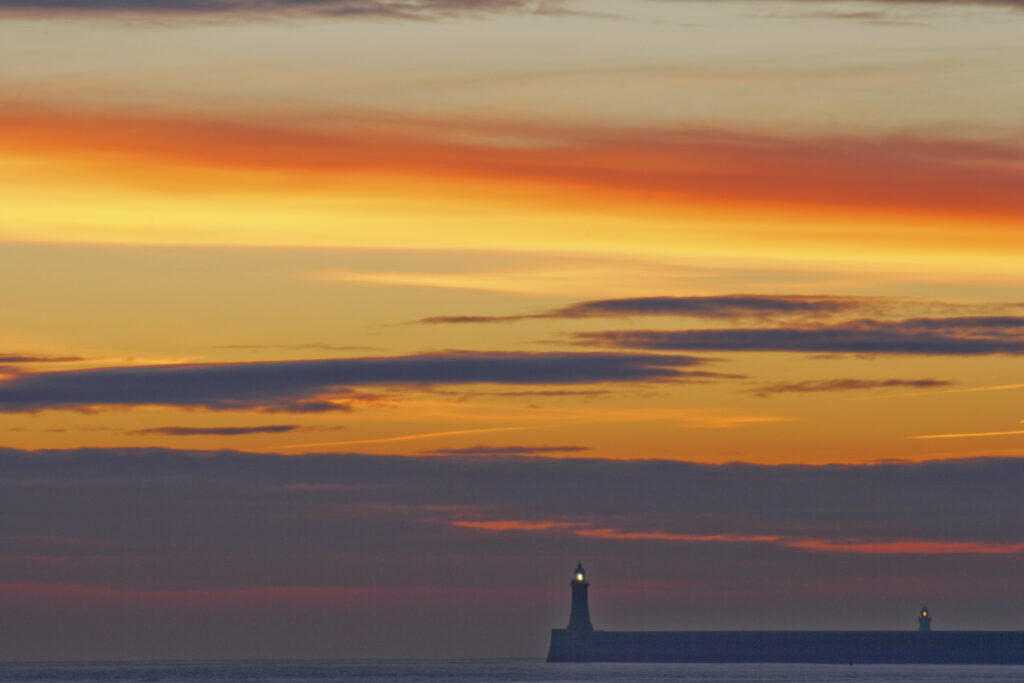 England, Tyne and Wear, Cullercoats. Sunrise looking towards the North Tyne Pier and lighthouse in Tynemouth