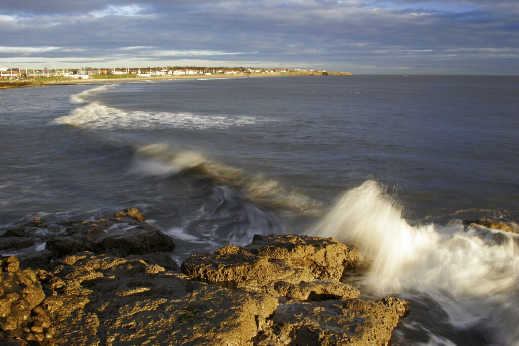 England, Tyne and Wear, Seaburn. The morning sun illuminates the crashing waves of the north sea looking across Whitburn Bay
