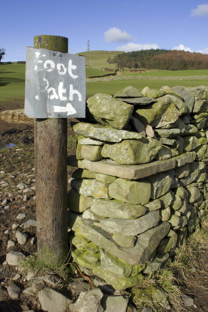 ENGLAND, Cumbria, Ulverston. Foot path sign and dry stone wall on route to Old Hall Farm, on the Cumbria Way