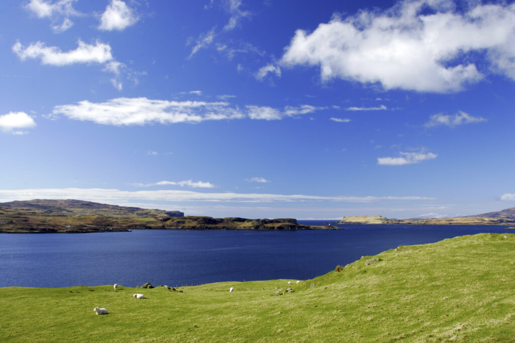 Scotland, The Isle of Skye, Loch Harport. The blue sky reflected in the waters of Loch Harport with surrounding green fields.