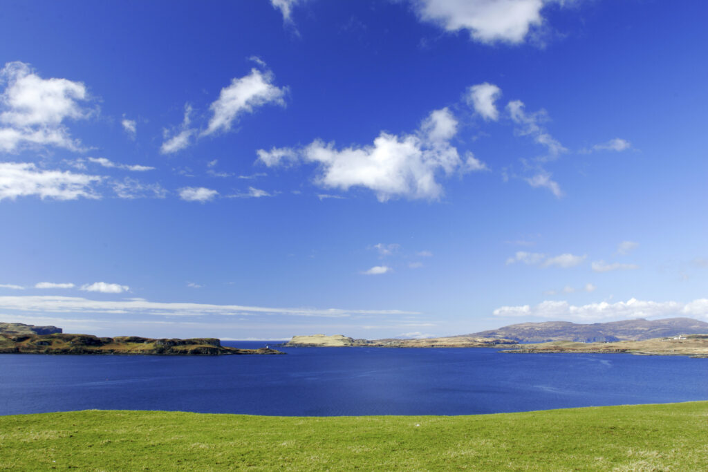 Scotland, The Isle of Skye, Loch Harport. The blue sky reflected in the waters of Loch Harport with surrounding green fields.