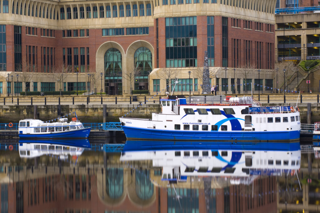 England, Tyne and Wear, Newcastle Upon Tyne. Newcastle Quayside and moored river cruise boats, reflected in the still waters of the Tyne.