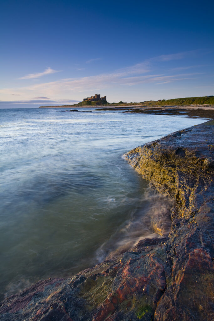England, Northumberland, Bamburgh. Bamburgh Castle, beach and dunes viewed shortly after sunrise from Harkess Rocks.