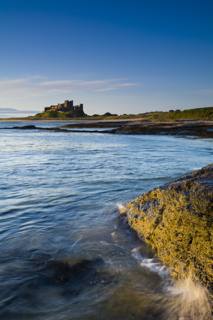 England, Northumberland, Bamburgh. Bamburgh Castle, beach and dunes viewed shortly after sunrise from Harkess Rocks.