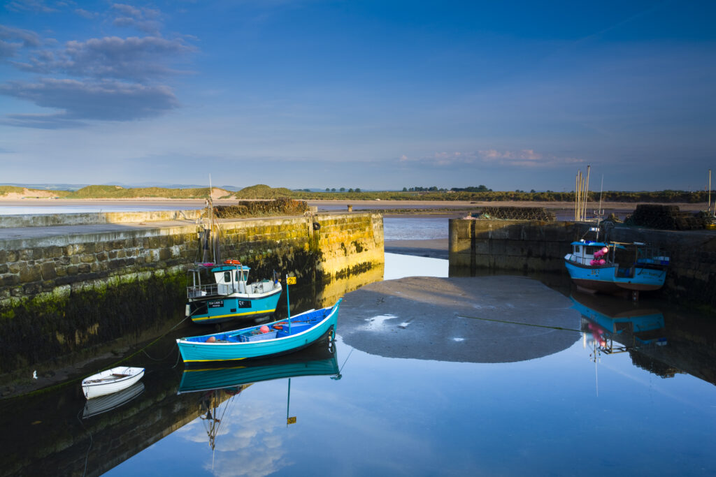 England, Northumberland, Beadnell. Boats moored within the Harbour Walls of the Beadnell Harbour - viewed at low tide.