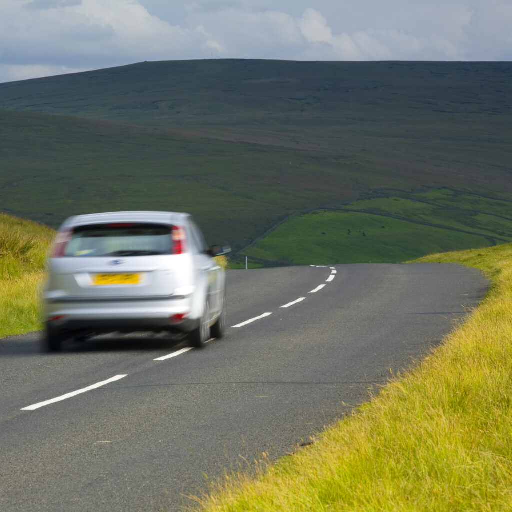 England, Northumberland, North Pennines. Car driving down a country road running through dramatic Pennine scenery, in the North Pennines Area of Outstanding Beauty.