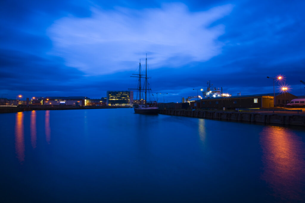 Scotland, Edinburgh, Leith. Boat moored at Leith Harbour with the Ocean-terminal shopping mall, a modern development on the Leith waterfront, in the distance.