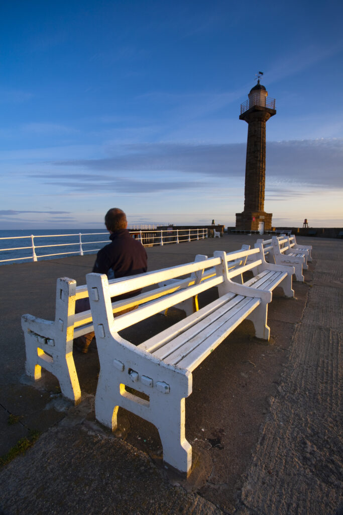 England, North Yorkshire, Whitby. Person sitting on a bench on the pier at Whitby.