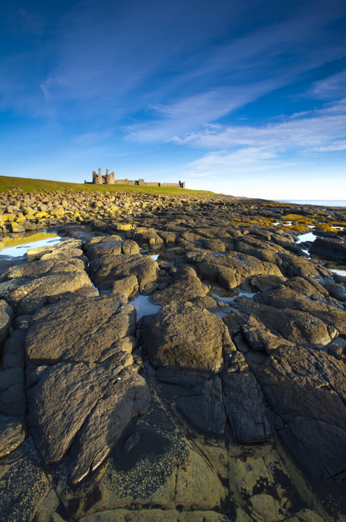 England, Northumberland, Dunstanburgh Castle. Dunstanburgh Castle and surrounding coastline at low tide, viewed from Cushat Stiel.