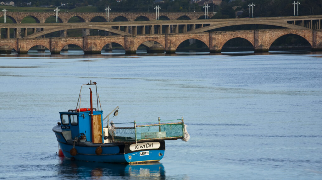 England, Northumberland, Berwick upon Tweed. Fishing boat moored upon the mouth of the River Tweed, with the Royal Border Bridge and the Royal Tweed Bridge in the distance.