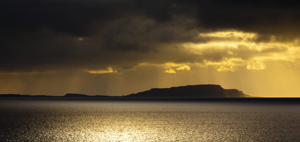 Scotland, Western Isles, Isle of Soay. Dramatic shafts of light from the settin sun above the Isle of Soay, viewed from Elgol on the Isle of Skye.