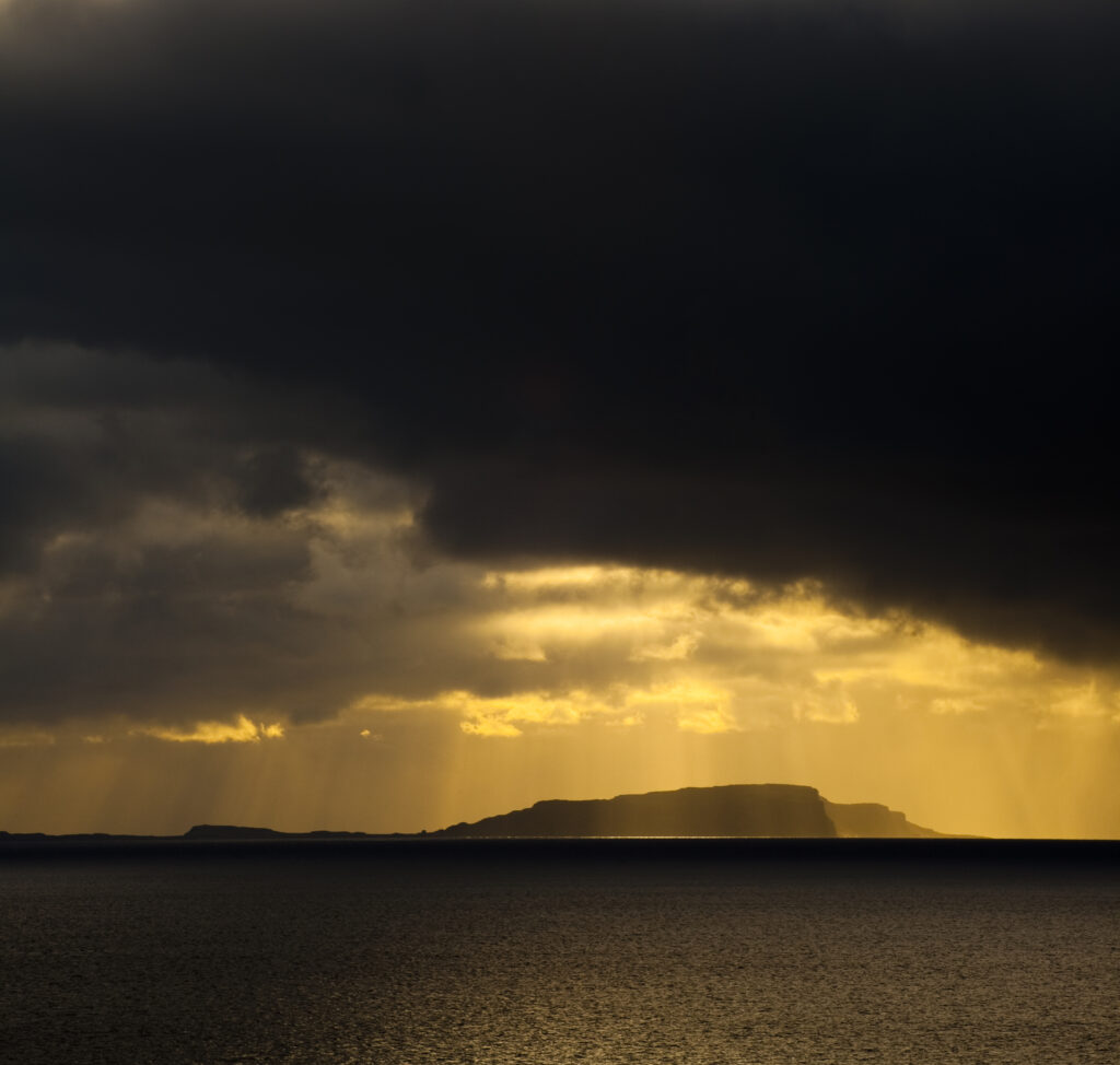 Scotland, Western Isles, Isle of Soay. Dramatic shafts of light from the settin sun above the Isle of Soay, viewed from Elgol on the Isle of Skye.