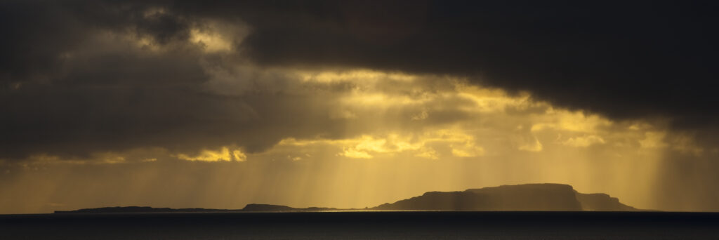 Scotland, Western Isles, Isle of Soay. Dramatic shafts of light from the settin sun above the Isle of Soay, viewed from Elgol on the Isle of Skye.