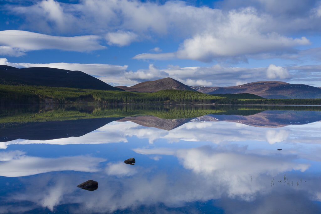 Scotland, Scottish Highlands, Cairngorms National Park. Clouds, forest and mountains reflected upon the still waters of Loch Morlich.