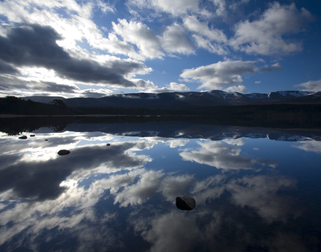 Scotland, Scottish Highlands, Cairngorms National Park. Dramatic clouds and Cairngorm mountains reflected upon the still face of Loch Morlich.