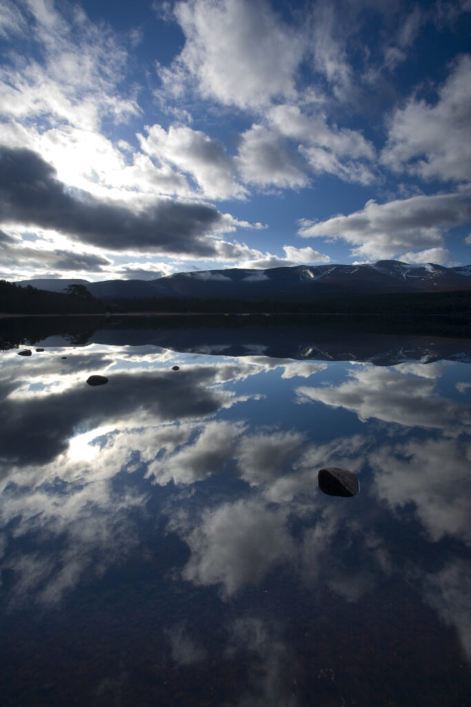 Scotland, Scottish Highlands, Cairngorms National Park. Dramatic clouds and Cairngorm mountains reflected upon the still face of Loch Morlich.