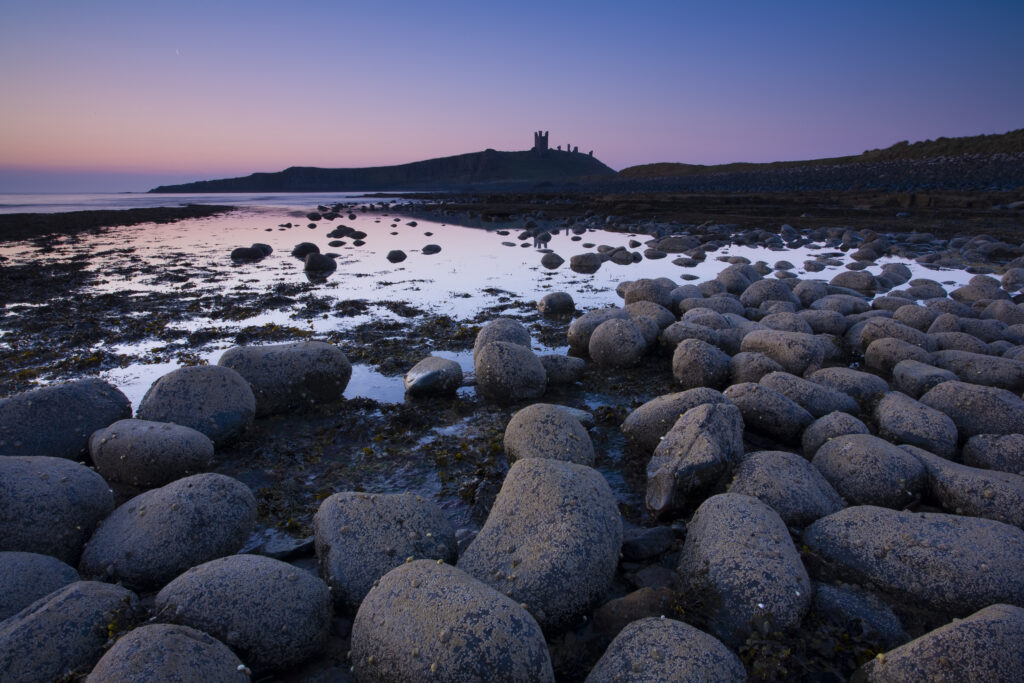 England, Northumberland, Embleton Bay. Weathered rocks dominate the low-tide shoreline of Embleton Bay