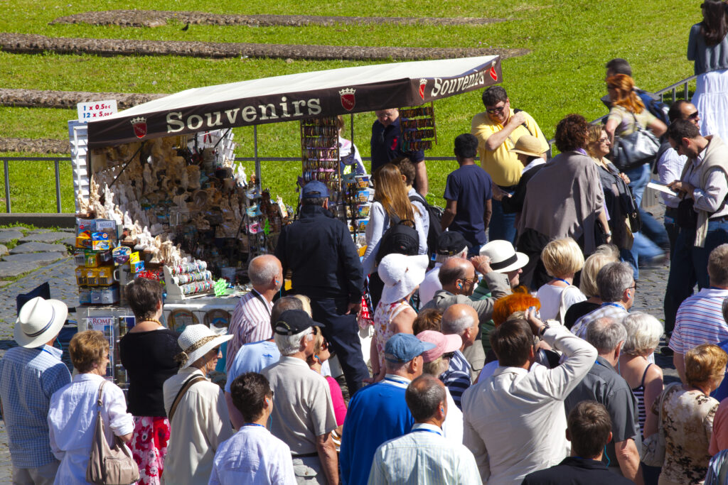Italy, Lazio, Rome. Tourists buying souvenirs from a stall by the Colosseum or Roman Coliseum, originally the Flavian Amphitheatre