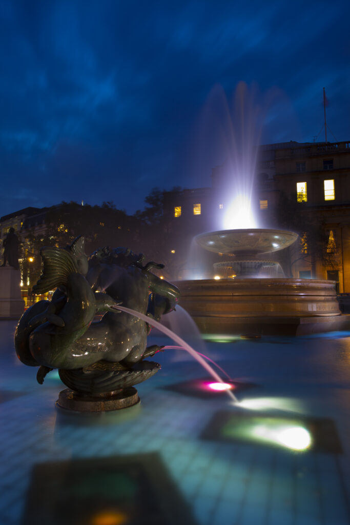 England, Greater London, City of Westminster. Flood lit fountains in Trafalgar Square, a popular tourist destination in London, photographed at dusk.