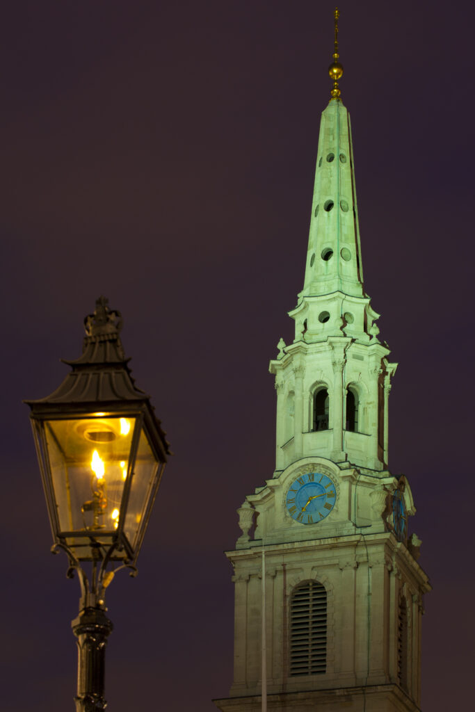 England, Greater London, City of Westminster. Flame lit street lamp and church spire near Trafalgar Square, a popular tourist destination in London, photographed at dusk.