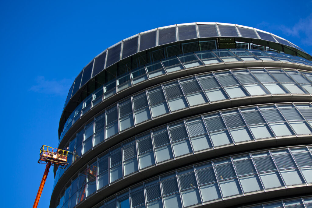 England, London, Southwark. Workman performing maintenance from a cherry picker on a window of the London City Hall located near Tower Bridge on the River Thames.
