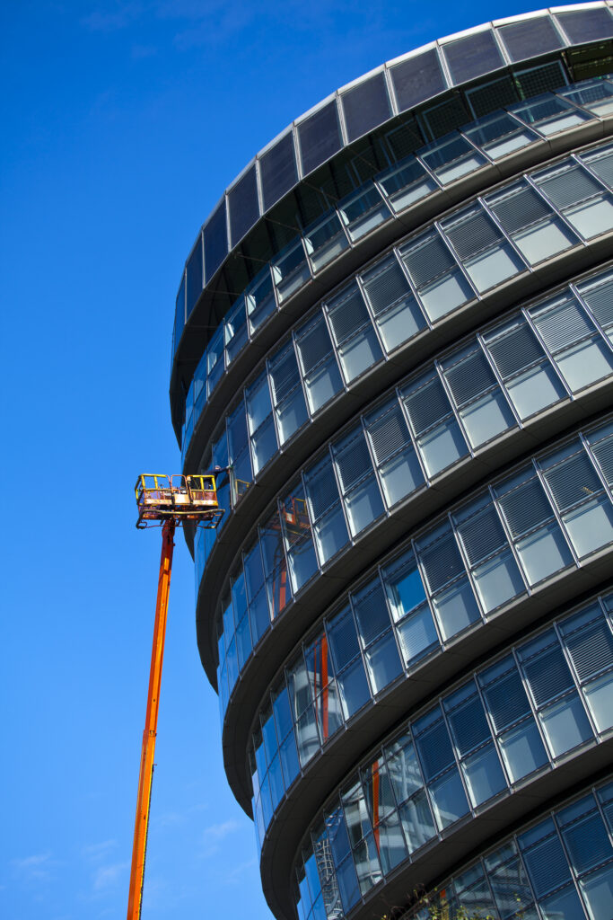 England, London, Southwark. Workman performing maintenance from a cherry picker on a window of the London City Hall located near Tower Bridge on the River Thames.