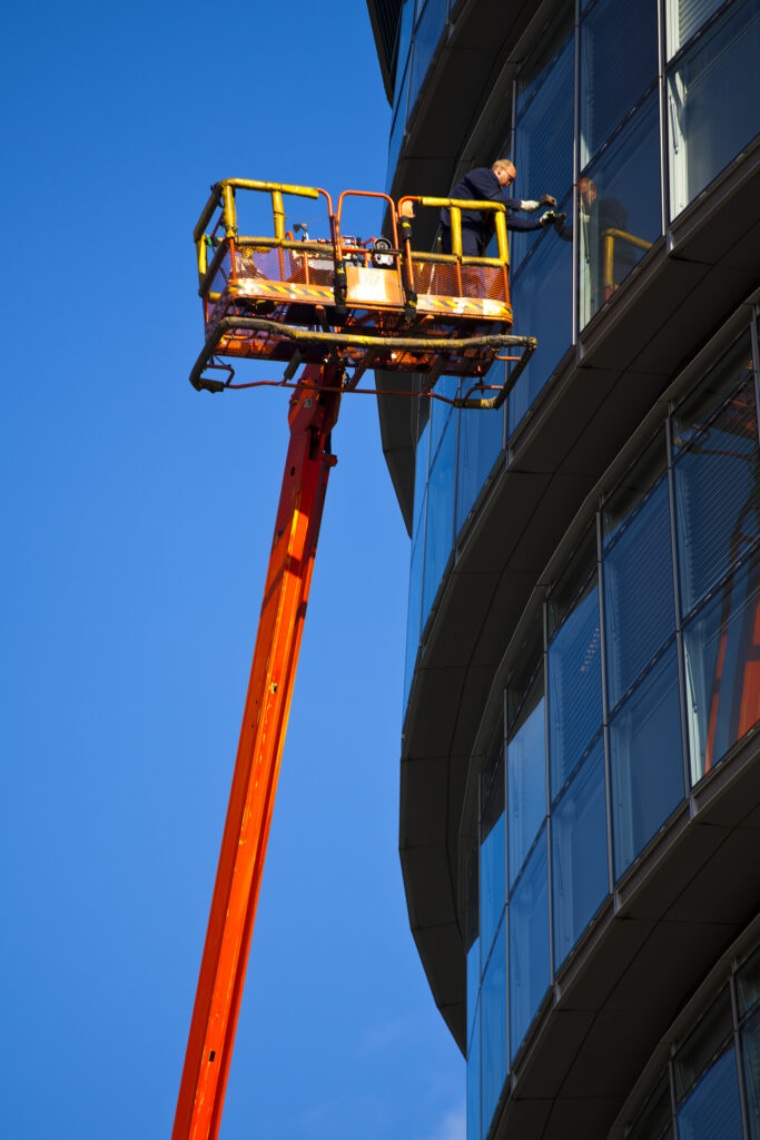 England, London, Southwark. Workman performing maintenance from a cherry picker on a window of the London City Hall located near Tower Bridge on the River Thames.
