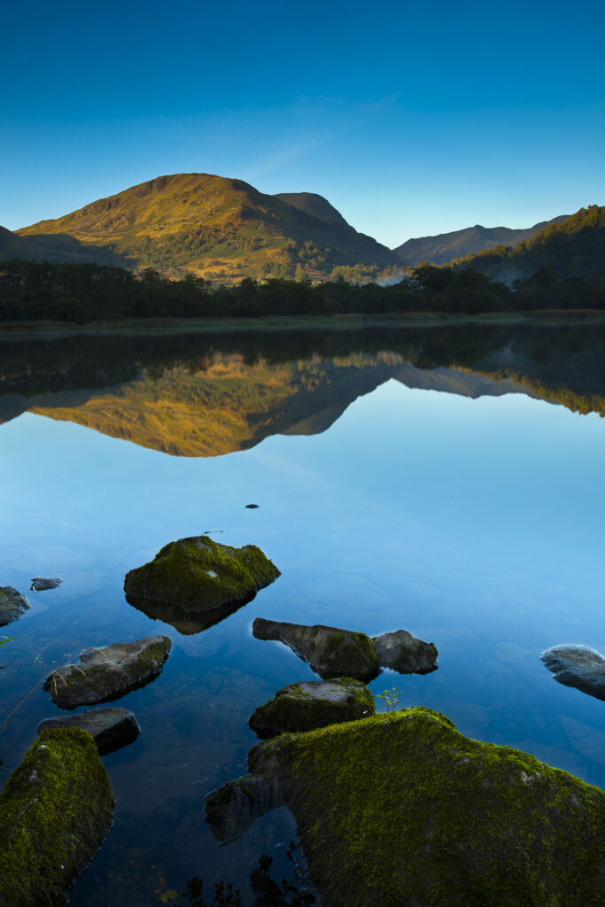 England, Cumbria, Lake District National Park. Helvellyn and surrounding mountain range reflected in still waters of Ullswater near Glenridding in Patterdale.