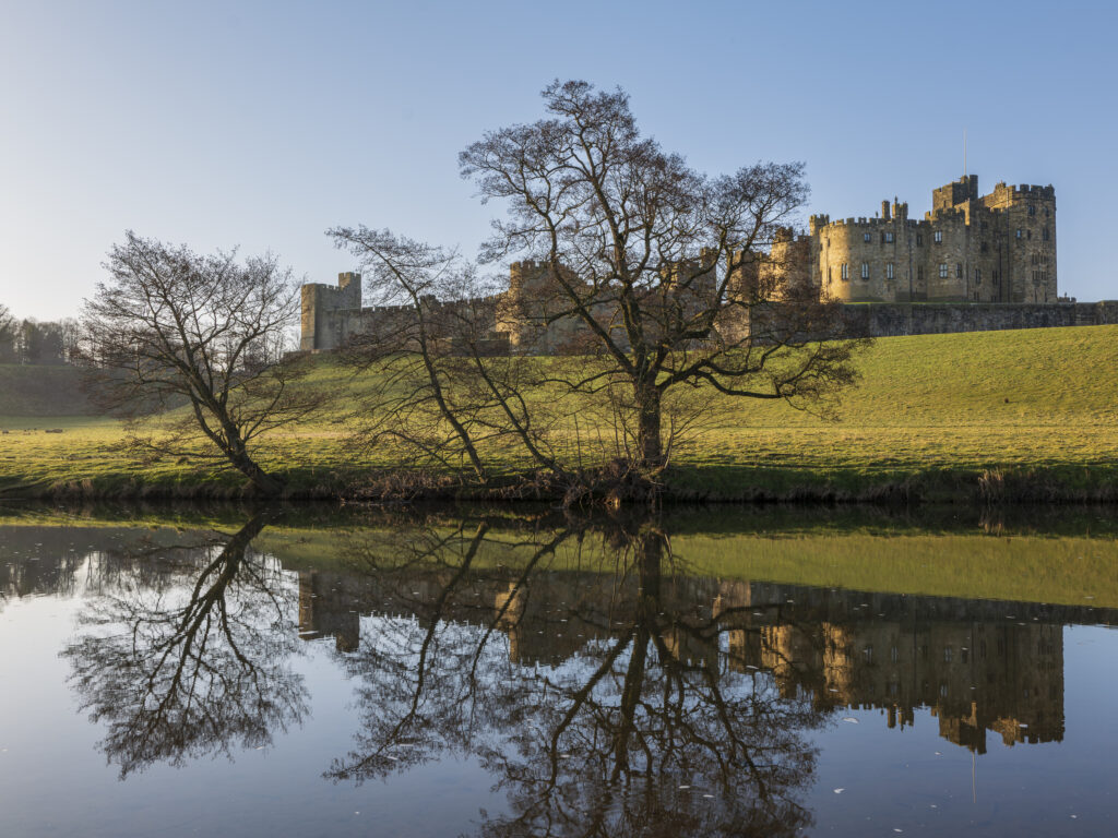 England, Northumberland, Alnwick. Alnwick Castle reflected in the still waters of the River Aln.