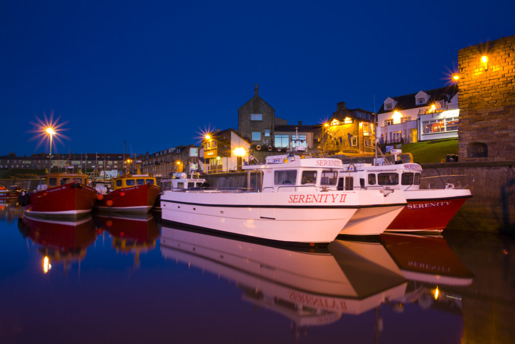 England, Northumberland, Northumberland Heritage Coast. Moored pleasure tour boats reflected in the still harbour waters of Seahouses.
