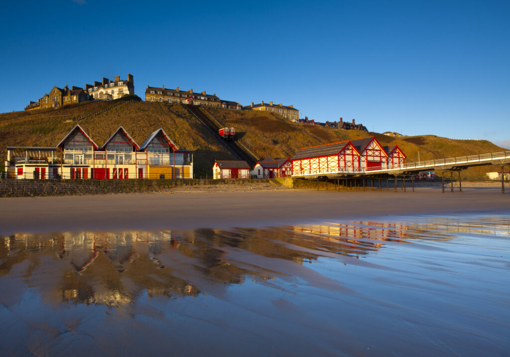 England, Cleveland, Saltburn-by-the-Sea. Looking across the north sea beach towards the funicular railway, one of the world's oldest water-powered cliff lifts, and the Victorian Pier.