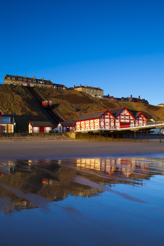 England, Cleveland, Saltburn-by-the-Sea. Looking across the north sea beach towards the funicular railway, one of the world's oldest water-powered cliff lifts, and the Victorian Pier.