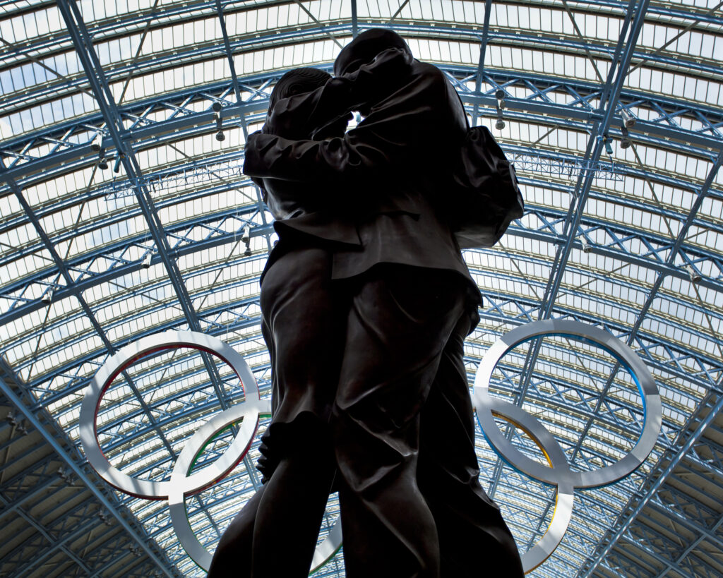 England, Greater London, London Borough of Camden. Statue beneath an Olympic sign celebrating the 2012 London Olympics on display in the London St Pancras Internationa railway station near King's Cross.