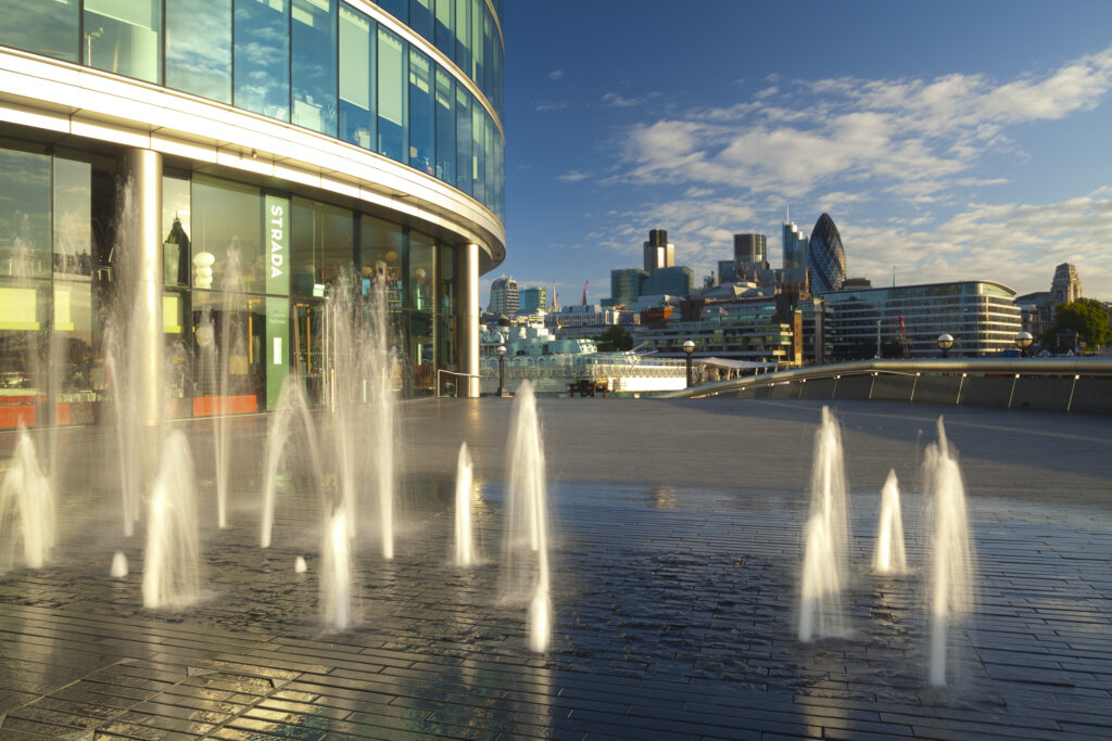 England, London, Southwark. Water fountains near the London City Hall and the 'More London' develpoment, looking towards the financial district of the City of London and the Gherkin.