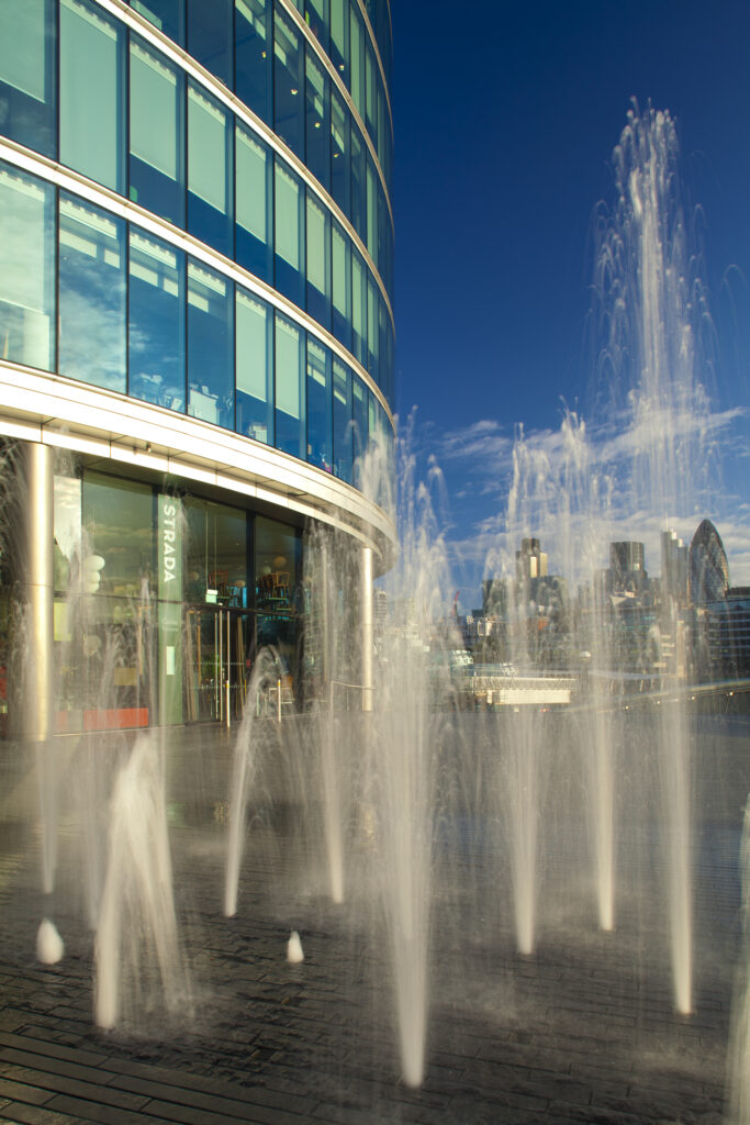 England, London, Southwark. Water fountains near the London City Hall and the 'More London' develpoment, looking towards the financial district of the City of London and the Gherkin.