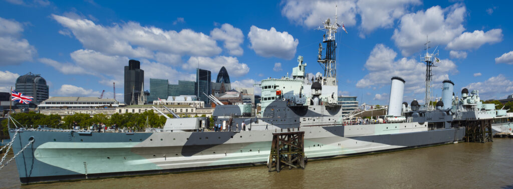 England, London, Southwark. HMS Belfast, originally a Royal Navy light cruiser, permanently moored in London on the River Thames with the City of London and the Gherkin in the distance.