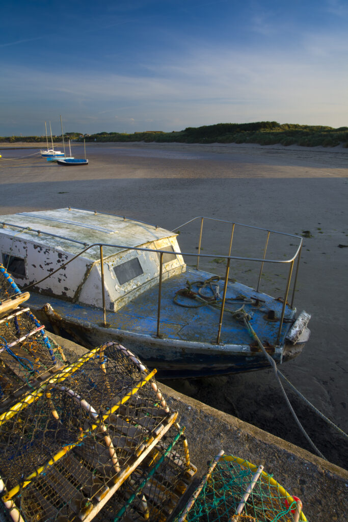 England, Northumberland, Beadnell. Lobster Pots and boat moored near the Harbour Walls of the Beadnell Harbour - viewed at low tide.