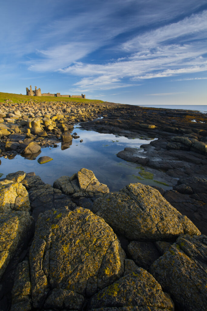 England, Northumberland, Dunstanburgh Castle. Dunstanburgh Castle and surrounding coastline at low tide, viewed from Cushat Stiel.